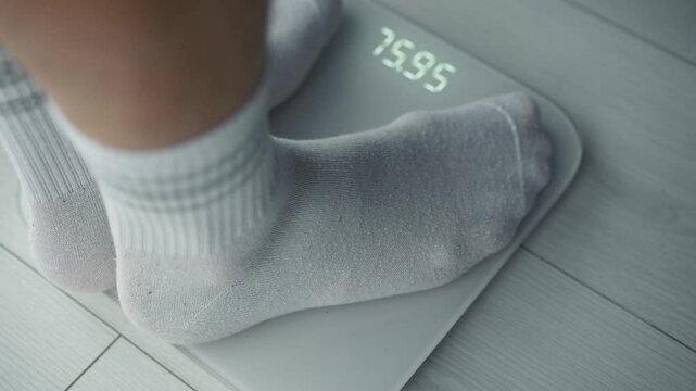 Close-up of a man on a scale.
Scales show a person his exact weight.
A man weighs himself on a scale in the morning in a bright room