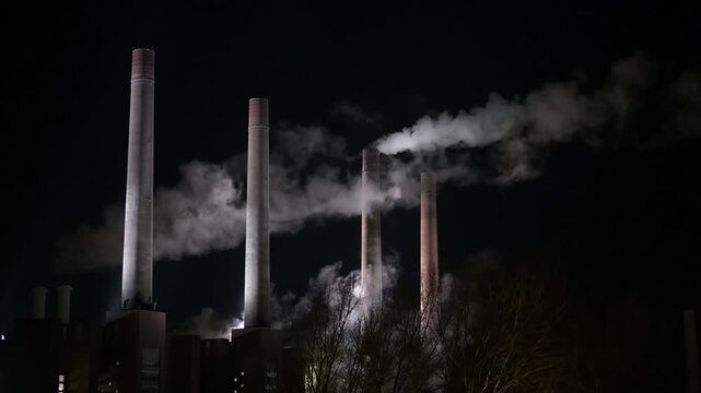 Smoking factory chimneys at night, illuminated by bright flashing spotlights. Wolfsburg, Germany