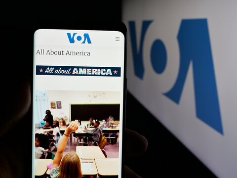 Stuttgart, Germany - 01-31-2025: Person holding mobile phone with web page of US broadcasting network Voice of America (VOA) on screen with logo. Focus on center of phone display.