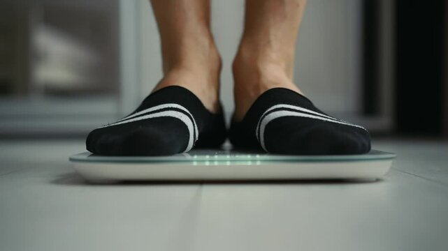 A man in black socks stands on a scale and measures his weight.
The man measures his weight.
A man watches his own weight