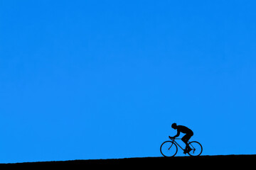 A man is riding a bicycle on a hill with a blue sky in the background