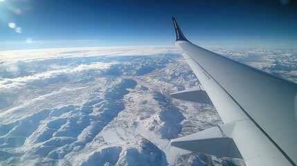 Fototapeta premium View from an airplane window of the wing and majestic snow-covered mountain ranges under a clear blue sky, evoking a sense of travel, adventure, and freedom—perfect for inspiration.