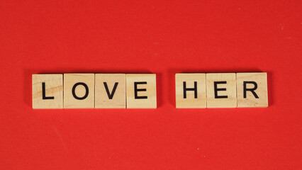 Wooden tiles spelling LOVE HER on a vibrant red background