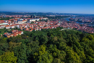 Fototapeta premium A panoramic cityscape view from a high vantage point, showcasing a sprawling city with red-roofed buildings, a large complex of structures, and a distant skyline under a clear blue sky.