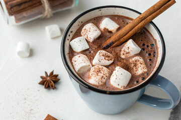 Top view of a steaming hot chocolate with marshmallows and cinnamon stick, served in a mug, isolated on white background