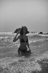 Fototapeta premium Frau kniend im Meer mit Wellen in schwarz weiß