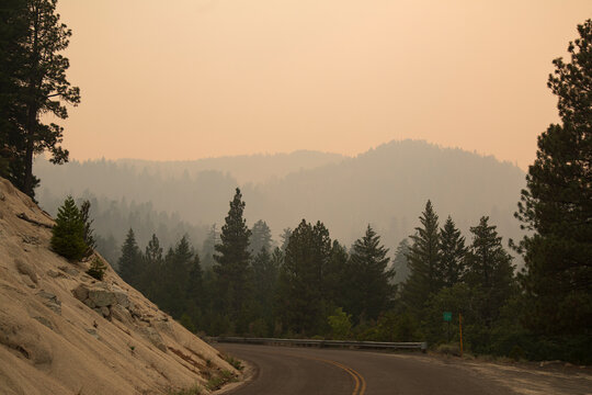 Janesville Grade in Lassen County, California, covered in thick smoke from the 2021 Dixie Fire, with hazy forested mountains in the background.