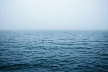 Obraz premium Serene Blue Ocean Water Under Soft Foggy Sky at Dawn