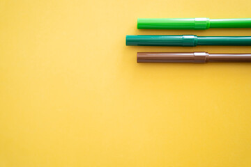 Lapiz rotulador  verde  y cafe para dibujar y escribir sobre fondo amarillo