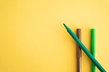 Lapiz rotulador  verde  y cafe para dibujar y escribir sobre fondo amarillo
