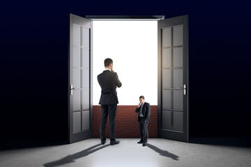 Fototapeta premium Businesspeople standing near giant open door with bright light, symbolizing decision-making or opportunity, in a dark background.