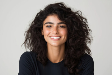 Fototapeta premium Young woman with curly hair smiling brightly in a neutral background setting