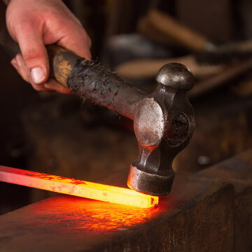 A basic hammer being used to strike and shape hot metal on an anvil in a blacksmiths forge