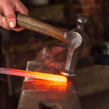 A shaped hammer being used to strike and shape hot metal on an anvil in a blacksmiths forge