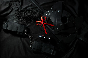 Sexy set of whip, cat mask, handcuffs and butt plug on black background