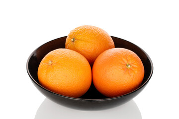 Three juicy oranges on a black ceramic plate, close-up, isolated on a white background.