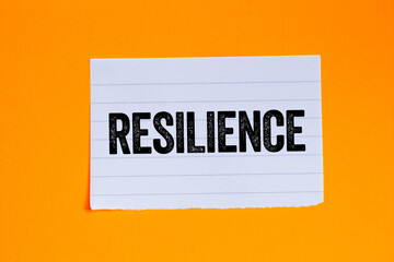 Resilience message written on ripped torn white paper piece on orange background. Conceptual resilience symbol. Copy space.