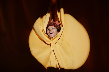 Woman with a beaming smile emerging through vibrant yellow fabric folds. The unique setting creates...