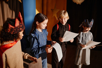Young students rehearsing for school play, some wearing costumes and holding scripts, happily...