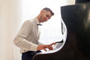 young guy in white shirt plays on old black piano, musician pianist performs melody on acoustic...