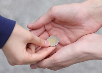 hand of the young woman while giving alms with a coin to the poor boy
