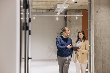 Businessman and businesswoman using tablet and discussing business strategy while walking in office corridor
