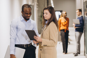 Professional colleagues analyzing project details, sharing insights through digital tablet in modern office hallway setting