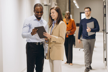 Business colleagues using a digital tablet while walking through a busy office corridor, discussing work related matters