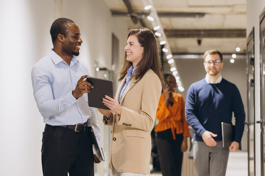 Professional team navigating modern workplace, collaborating using digital tablet while moving through sunlit corporate hallway