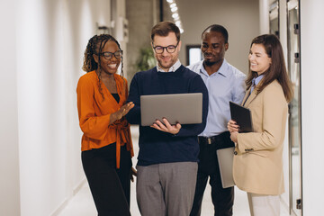 Diverse colleagues discussing work, using laptop and sharing ideas in a modern office corridor