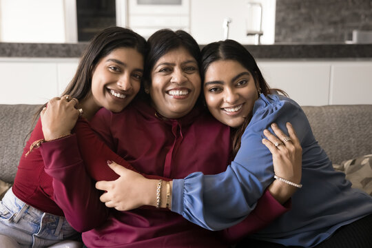 Older mother enjoy moment of tender hugs with two grown-up daughters, posing for camera with joyful expression, showing unity, giving support, feeling unconditional affection and love. Family portrait