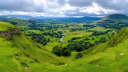 Obraz premium Panoramic valley view from high ground, lush green landscape, cloudy sky. Possible use Nature travel stock photo