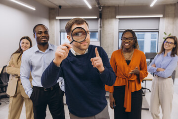 Businessman holding magnifying glass having an idea, standing with his multi ethnic business team in a modern office