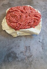 A portion of freshly minced beef arranged on paper atop a concrete table, highlighting negative space, presented in portrait view.