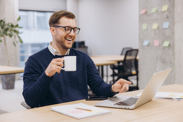 Professional businessman sipping coffee while typing on laptop during workplace relaxation moment