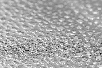 Photo of a light metal sheet with a texture similar to water droplets. Selective focus on shiny details and reflective surface.