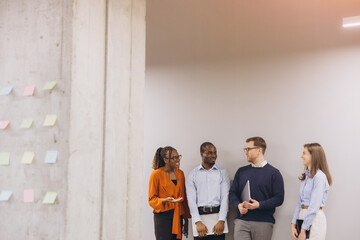 Diverse business team brainstorming near sticky note wall, collaborating dynamically in modern...
