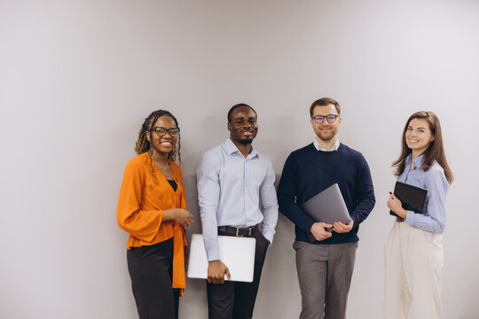 Diverse business team standing together in corporate workspace, working collaboratively with laptops, displaying professional unity and shared goals