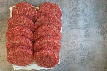 Raw beef burgers rested on paper atop a concrete table, captured from above. Negative space.