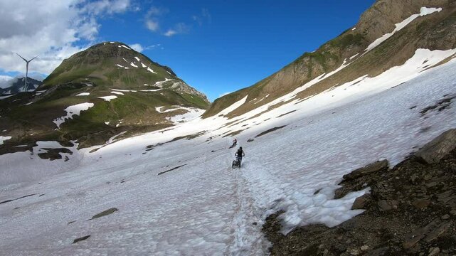 Due mountain biker spingono le MTB tra i nevai alpini verso il Passo del Gries, Val Formazza