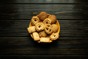A round yellow plate filled with an inviting variety of homemade cookies sits on a dark wooden surface