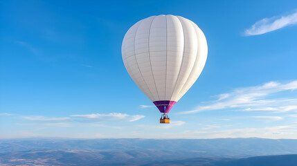 Fototapeta premium White hot air balloon floats high in the blue sky over a scenic mountain landscape during a sunny day.