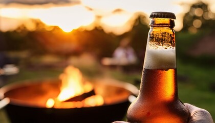A person enjoys a cold bottle of beer while sitting around a firepit. The warm glow of sunset creates a perfect backdrop for relaxation and camaraderie