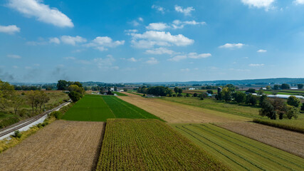 Expansive fields divided by green crops and brown earth stretch towards distant hills under a clear blue sky.