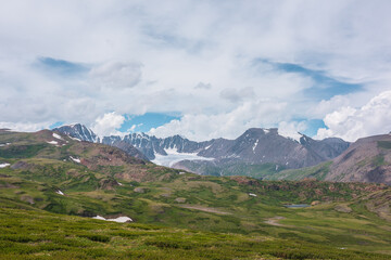 Scenic alpine landscape with green hills and rocks with view to big glacier and large snow-capped...