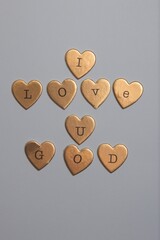 gold heart-shaped objects arranged to spell "I LOVE U GOD" on a gray background. © Elvis