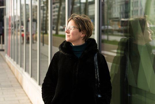 Portrait of a thirty year old attractive woman with a black winter coat reflecting in the glass of a modern office building