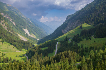 Fototapeta premium The Kaunertal glacier road curves through the mountains, leading down through the valley. A thick covering of trees, primarily evergreen, covers the lower and middle sections of the valley