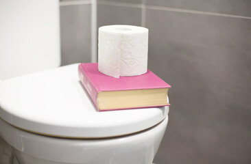 Book and Toilet Paper on Toilet Seat Traditional Reading Habit Concept