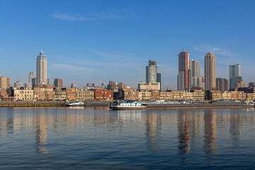 Naklejka premium Skyline with skyscrapers of Rotterdam with in the foreground typical dutch architecture with brick facades of a few stories high. cargo ships in the maashaven.